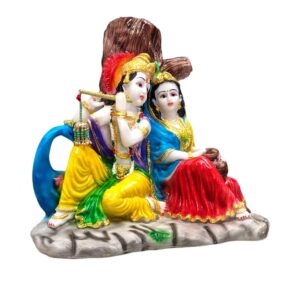 Side view of Radha Krishna Idol sitting besides each other in front of a tree listening to the blissful tones of Krishna flute