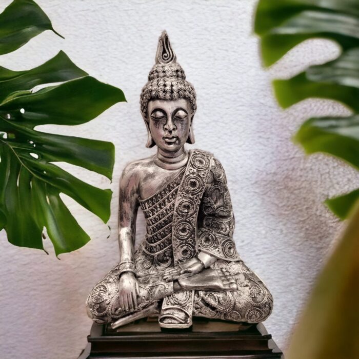 Image of a silver oxidized meditating Buddha statue placed on a wooden platform in a living room setting