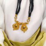 Two Wati Mangalsutra necklace with gold plating and black bead chain, laid flat on a white velvet pad.