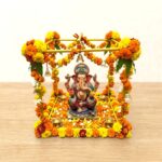 Gold finish metal Ganpati makhar frame decorated with marigold garlands and a home Ganesh idol
