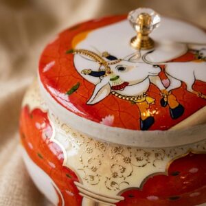 Close-up of red pichwai cow and lotus art on metal dry fruit jar