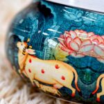 Close-up of pichwai cow and lotus art on metal dry fruit jar