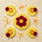 Yellow flower rangoli diya set of 5 laid out as a rangoli, with a 7 inch maroon rose centrepiece and four 4 inch diyas holding lit rose tealight candles.
