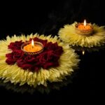 7 inch and 4 inch yellow flower rangoli diyas lit on a reflective black surface, showing the size difference between the centrepiece and the smaller pieces.