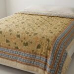 Jaipur hand block-printed cotton Razai quilt spread across a bed in yellow botanical print