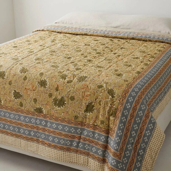 Jaipur hand block-printed cotton Razai quilt spread across a bed in yellow botanical print