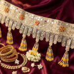 Golden sheesha toran detail on maroon silk — mirror lace, pearl and marigold yellow tassels with red beaded flowers, styled for haldi and wedding