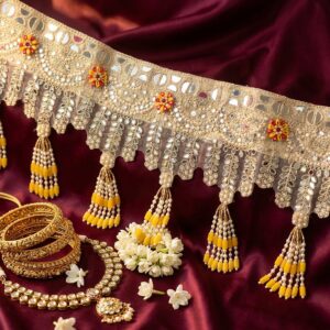 Golden sheesha toran detail on maroon silk — mirror lace, pearl and marigold yellow tassels with red beaded flowers, styled for haldi and wedding