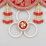 Pearl loop medallion and red bead tassels hanging from scalloped edge of red embroidered toran