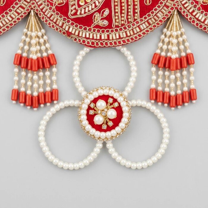 Pearl loop medallion and red bead tassels hanging from scalloped edge of red embroidered toran