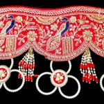 Close up of red gota patti toran peacock embroidery gold zari sequins pearl medallion and red bead tassel