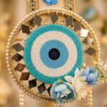 Close-up of hand-beaded evil eye motif in turquoise and blue seed beads, ringed with gold-framed glass mirror diamonds