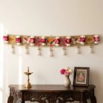 Golden Shubh Labh bandhanwar toran hanging on a wall, 40 inch embroidered door hanging with pink and white roses, pearl tassels, Ganesha and elephant motifs, styled with brass diya for Diwali decor